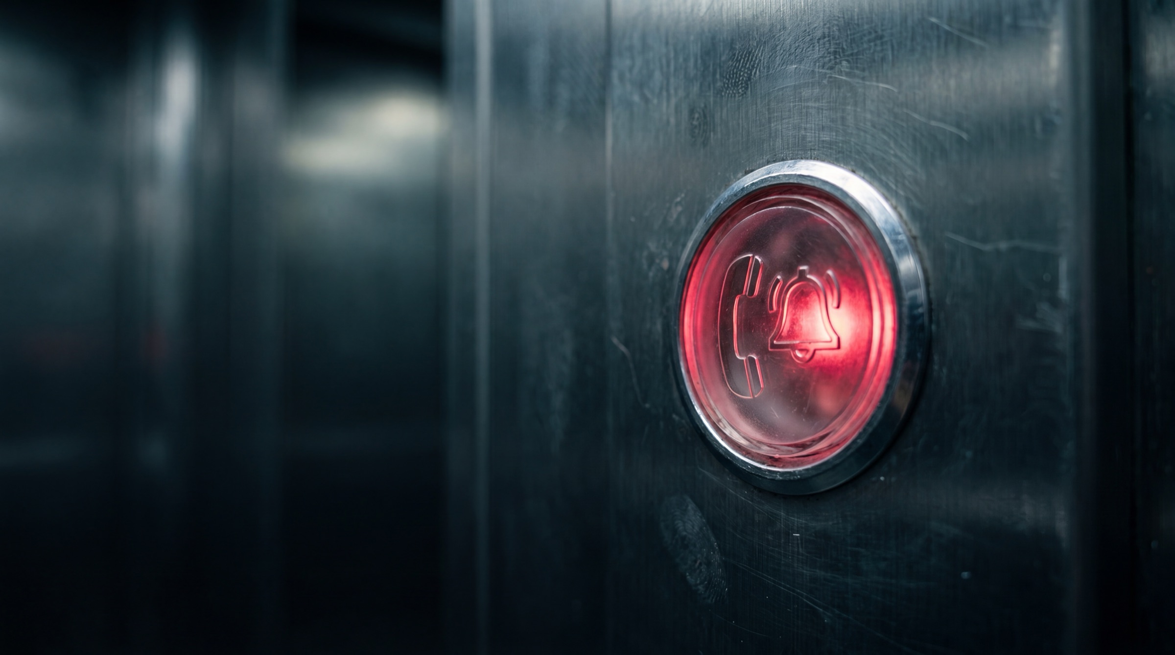 Illuminated red lift emergency call button engraved with a phone and bell symbol on a brushed steel panel